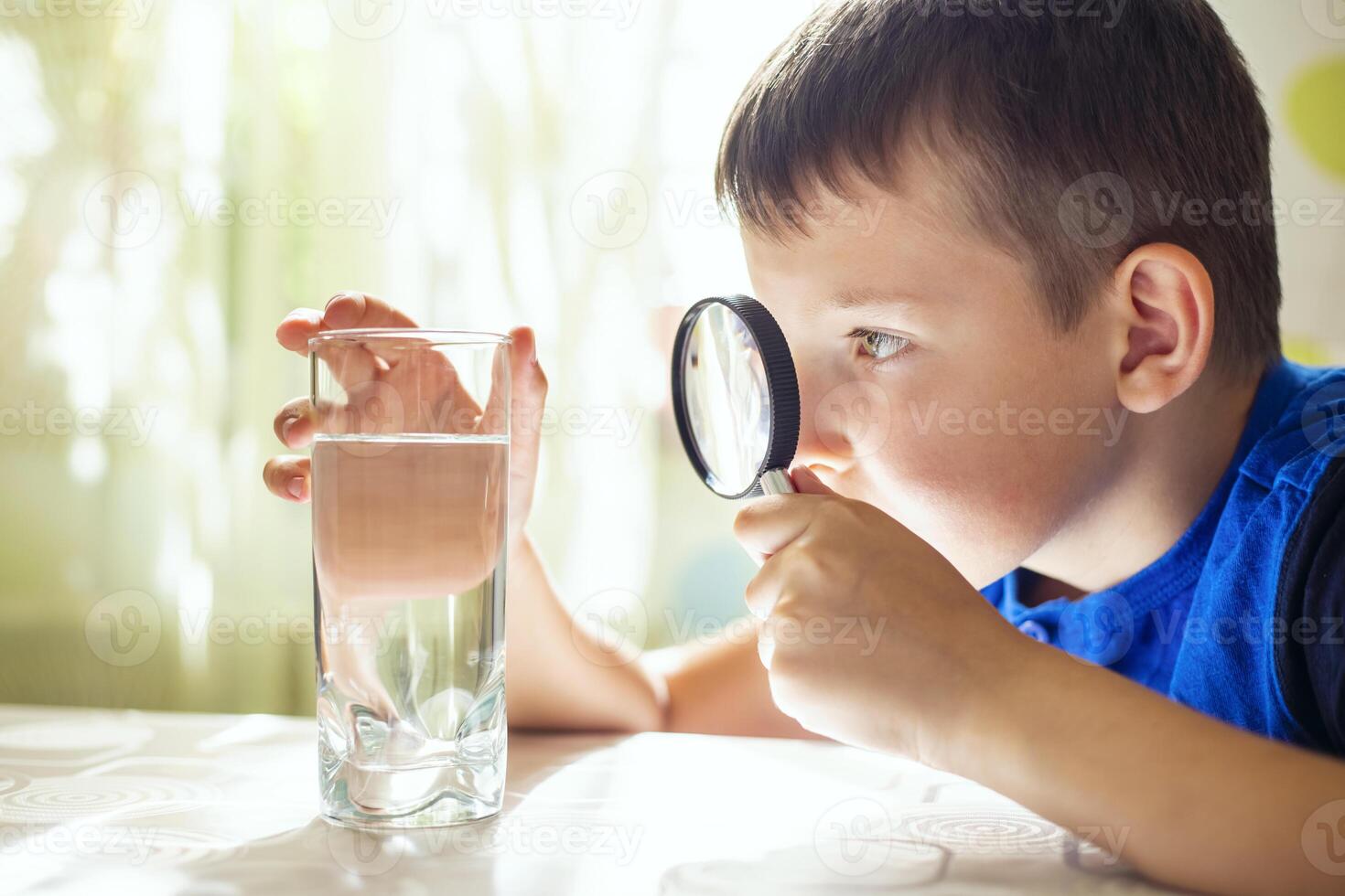 The child boy looking at water in a glass through magnifying glass photo
