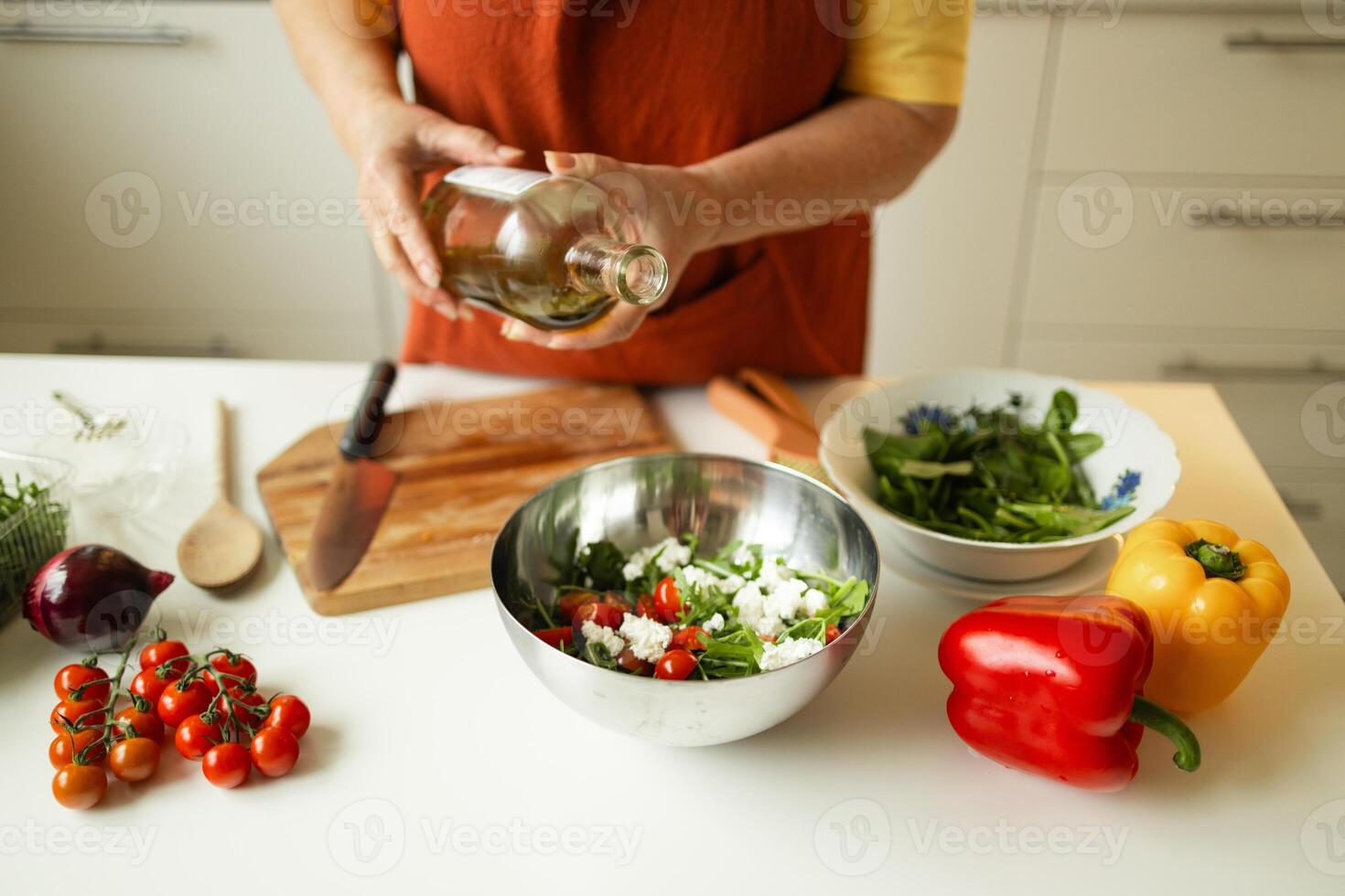 Female chef in a uniform pours olive oil from a bottle. Caucasian female food blogger working explaining how to cook a dish photo