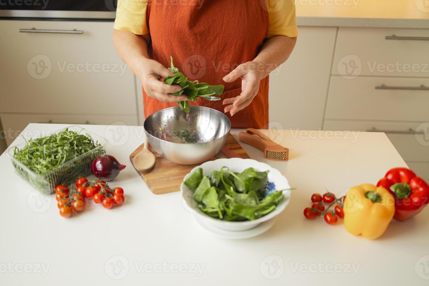 Senior 60s blond smiling woman holding a knife and fresh spinach whole preparing a bowl of healthy diet salad in her rustic eco kitchen photo