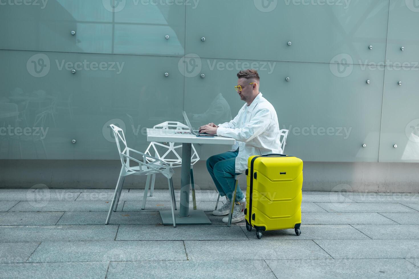 Happy traveling Caucasian man in stylish clothes uses mobile smartphone and laptop, checking trip destination on Internet. Male waiting at flight gates for plane boarding, smiling have a vacation trip photo