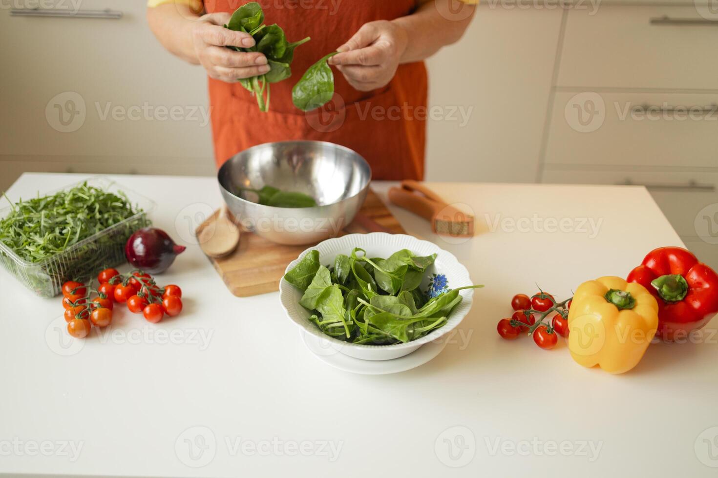 Senior 60s blond smiling woman holding a knife and fresh spinach whole preparing a bowl of healthy diet salad in her rustic eco kitchen photo
