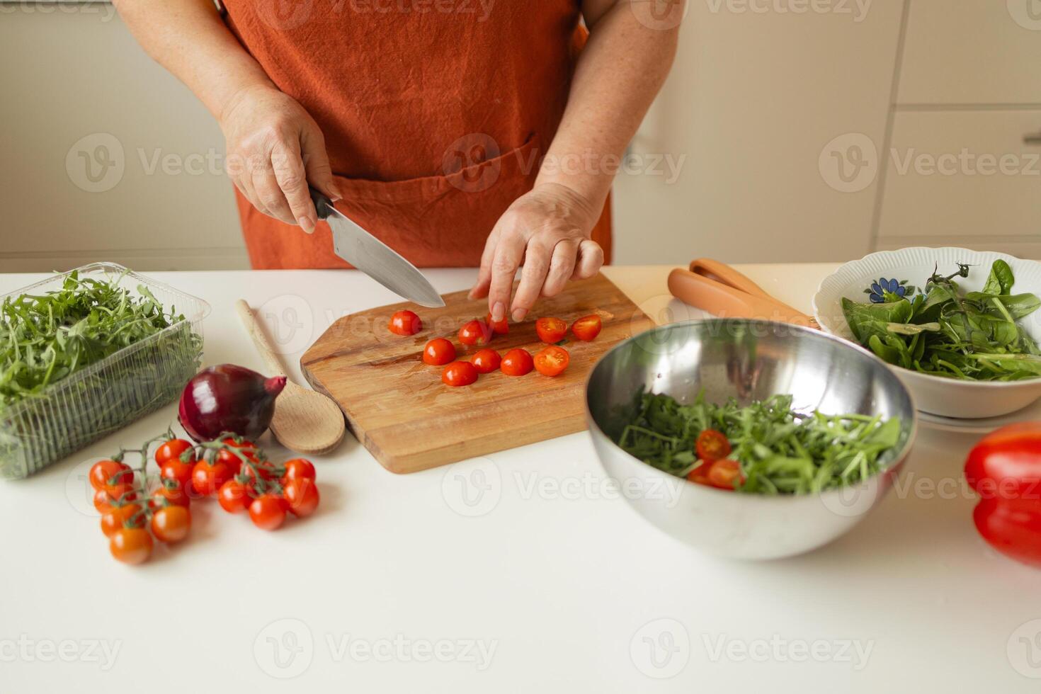 Hands of senior 60s female chopping fresh tomato on wooden board while preparing italian salad with vegetables photo