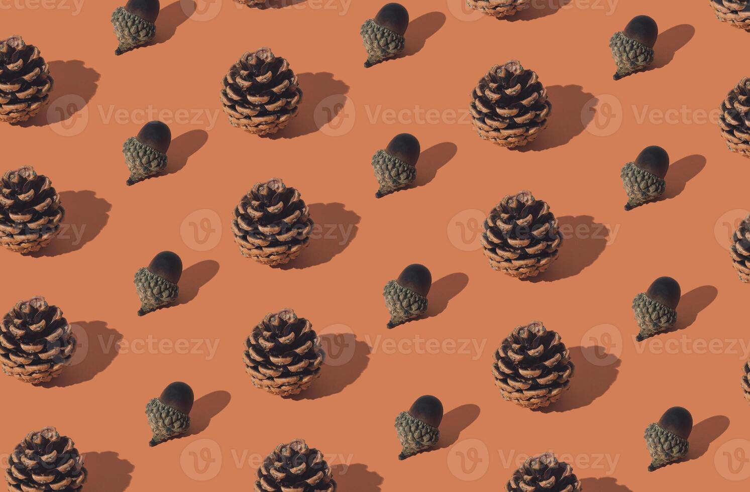 Trendy autumn or fall pattern made with pinecones and acorns or oak nuts on orange background. Minimal autumn objects composition. Nature flat lay. Season concept. photo