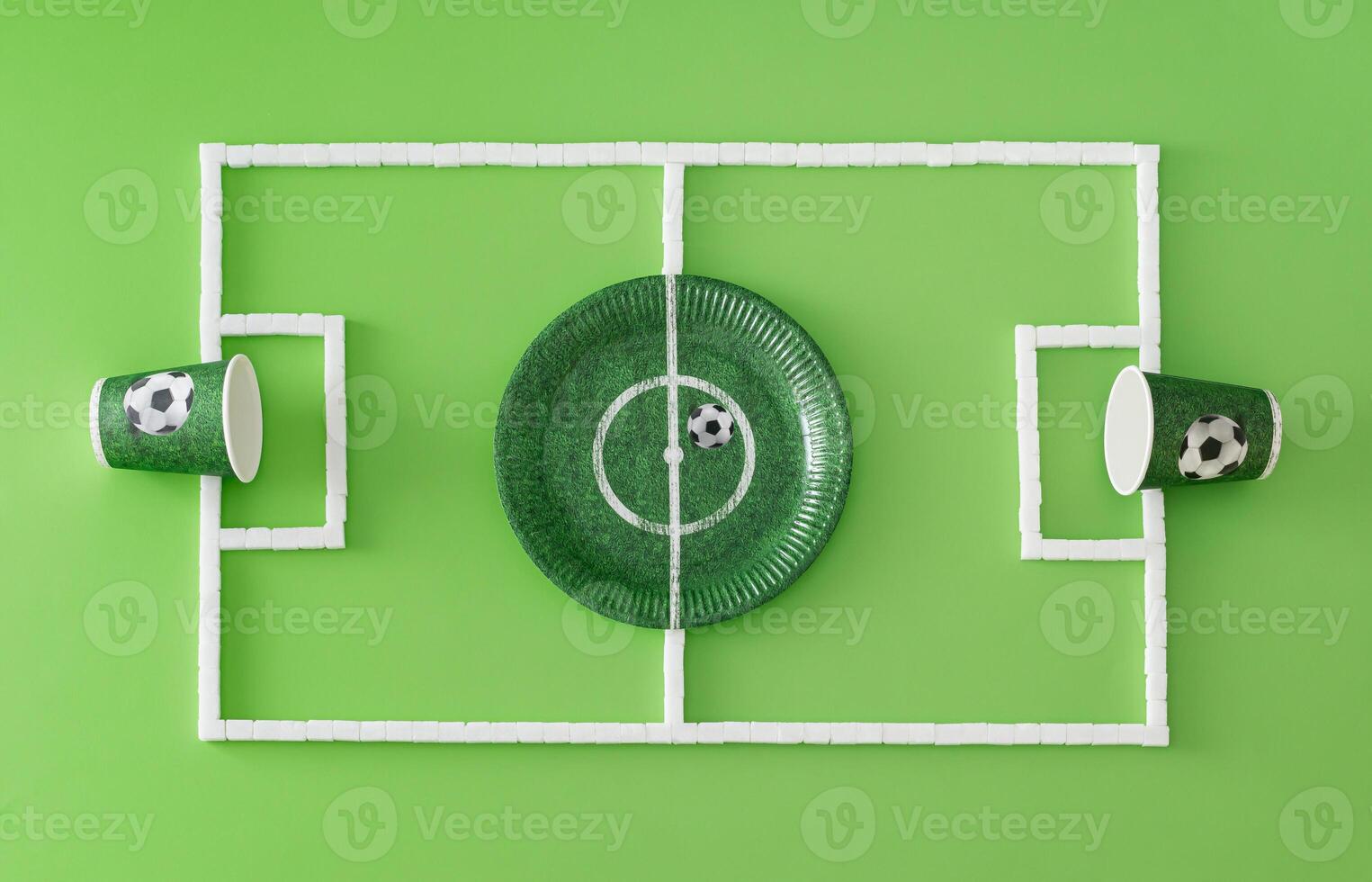 Football pitch or soccer field made with paper cups and plate and sugar cubes on light green background. Minimal sport or food concept. Creative football party composition. Flat lay, top of view. photo