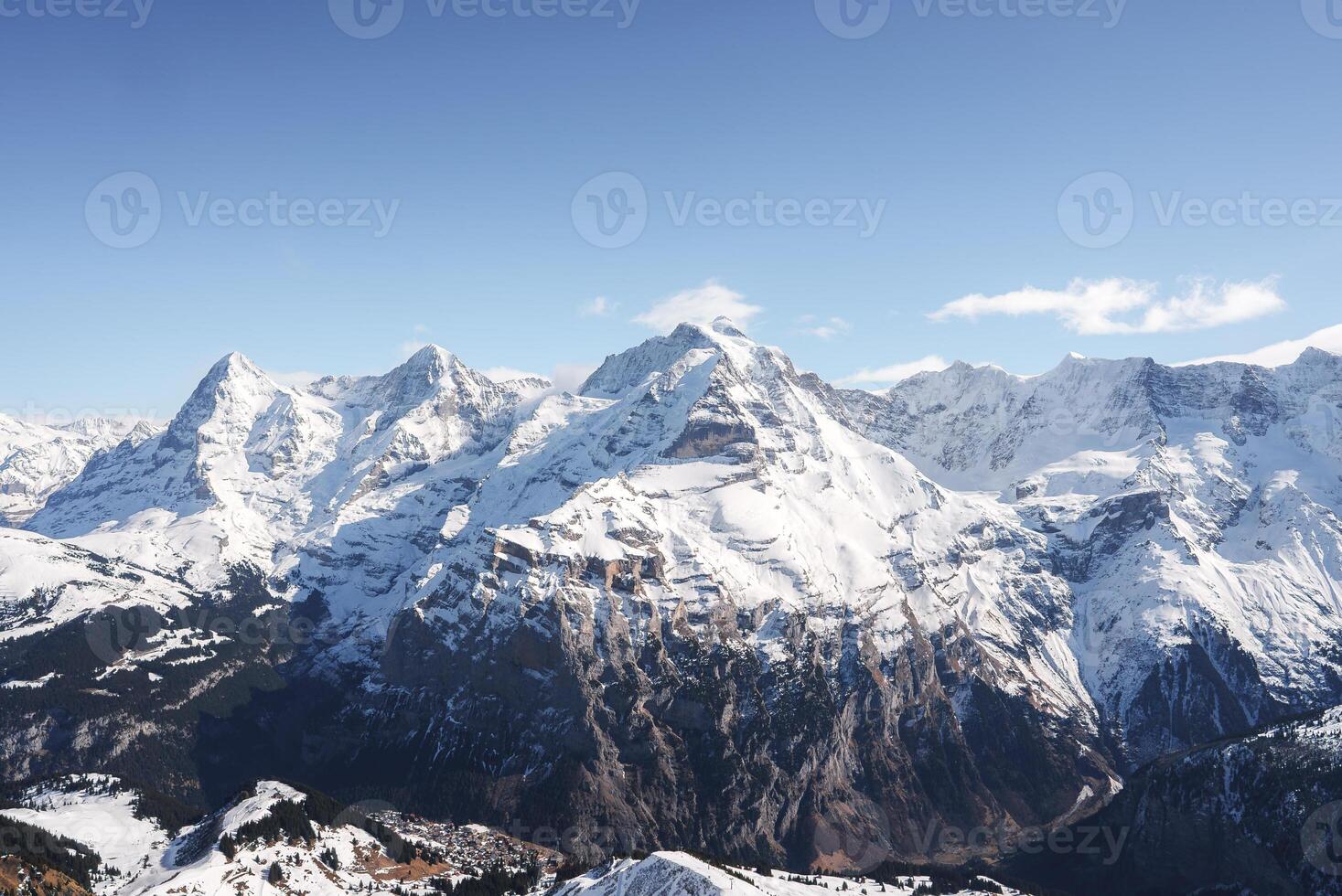 Experience the awe inspiring Swiss Alps with snow covered peaks and rugged slopes captured from the Murren ski resort. Majestic mountains under a clear blue sky create a dramatic alpine scene. photo