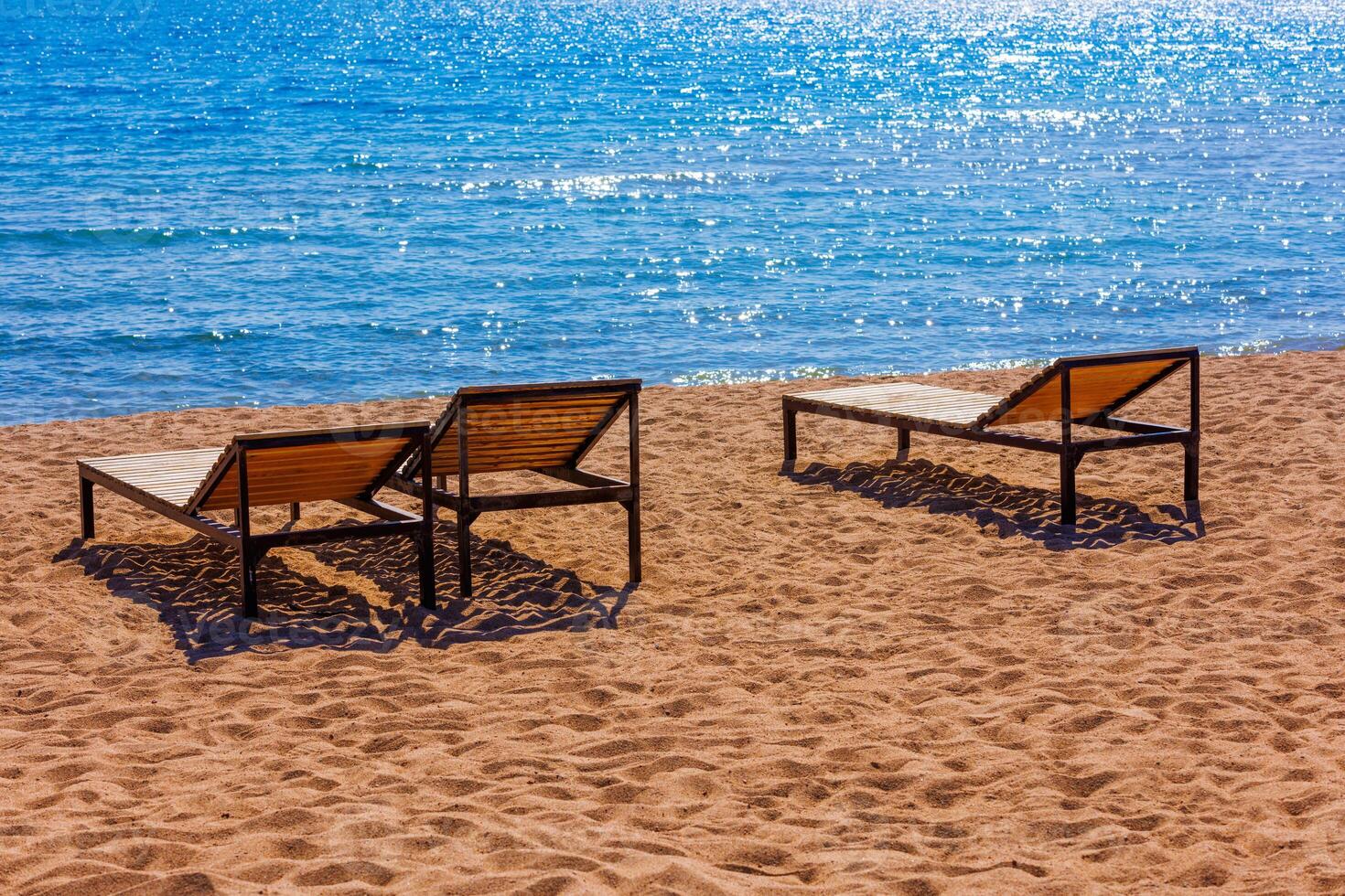 empty outdoor lounge chairs on sandy beach near blue water. photo