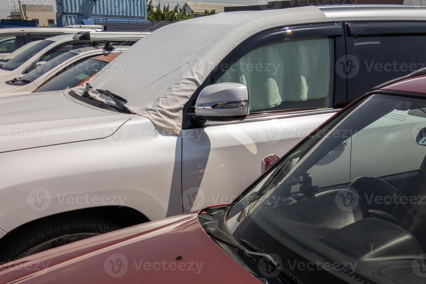 car windshield is covered with white bedsheet to prevent heating on a parking lot at hot sunny summer day in Asia photo