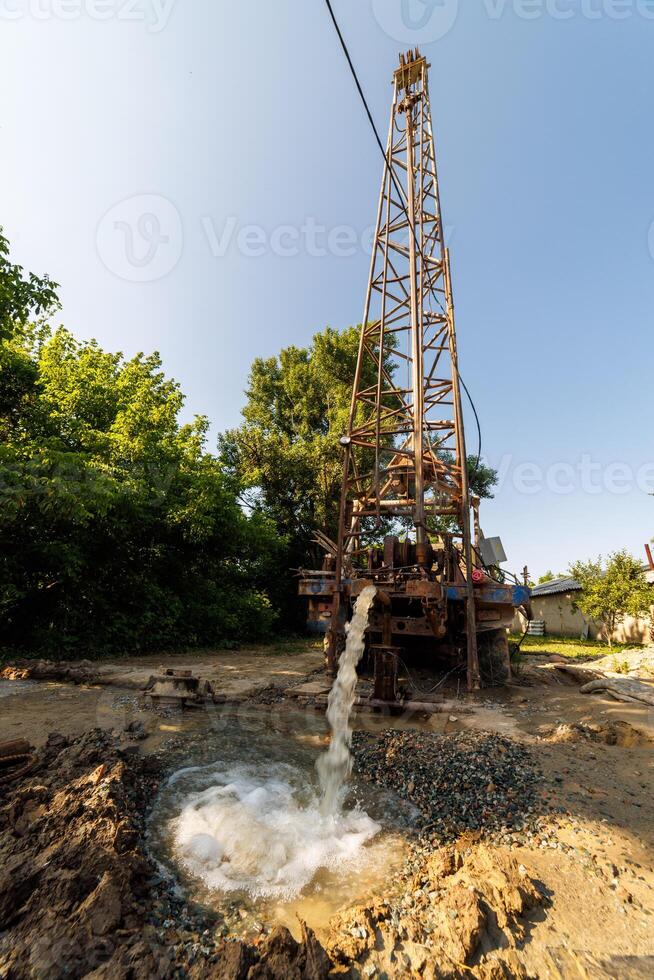 old water pump truck extracts water from a hole in the ground at sunny summer day photo