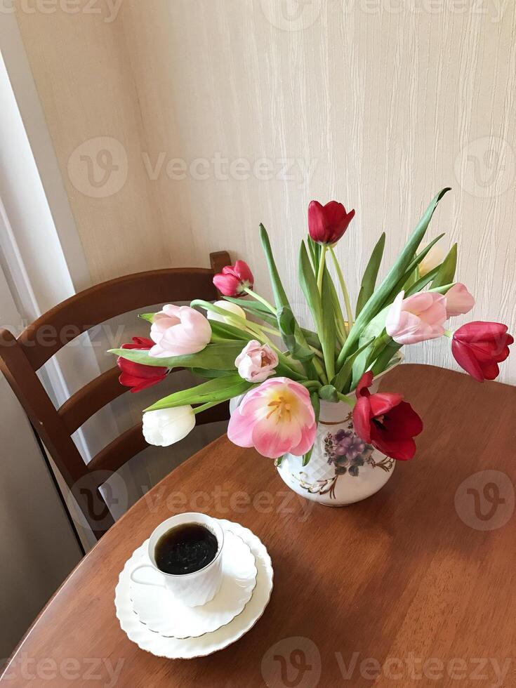 Tulips in a vase and a cup of coffee on a table photo