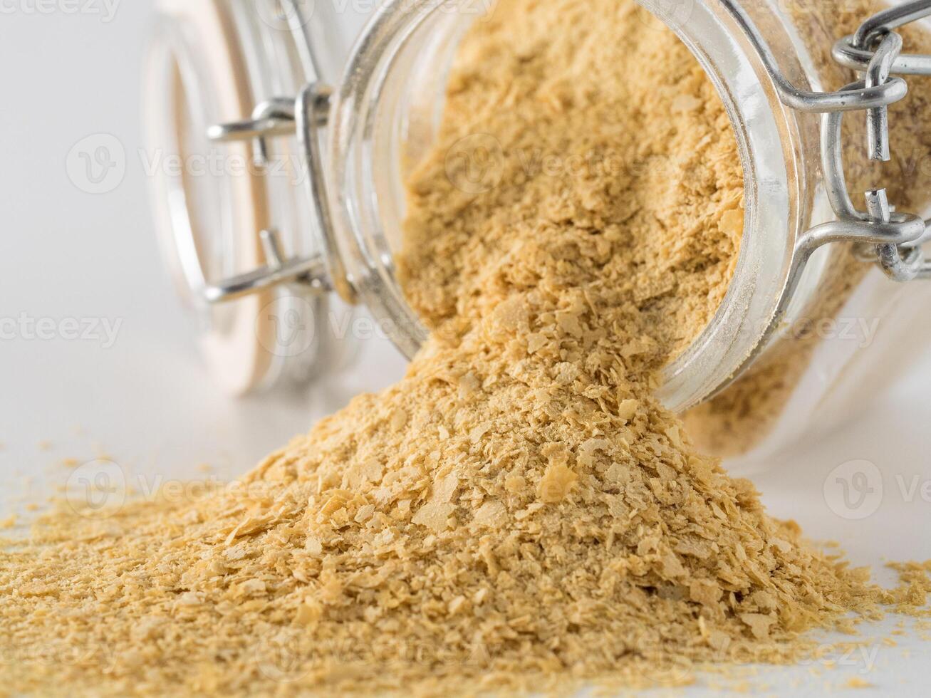 Nutritional yeast background. Nutritional inactive yeast spilled from glass jar on white background. Copy space.Side view.Nutritional yeast is vegetarian superfood with cheese flavor, for healthy diet photo