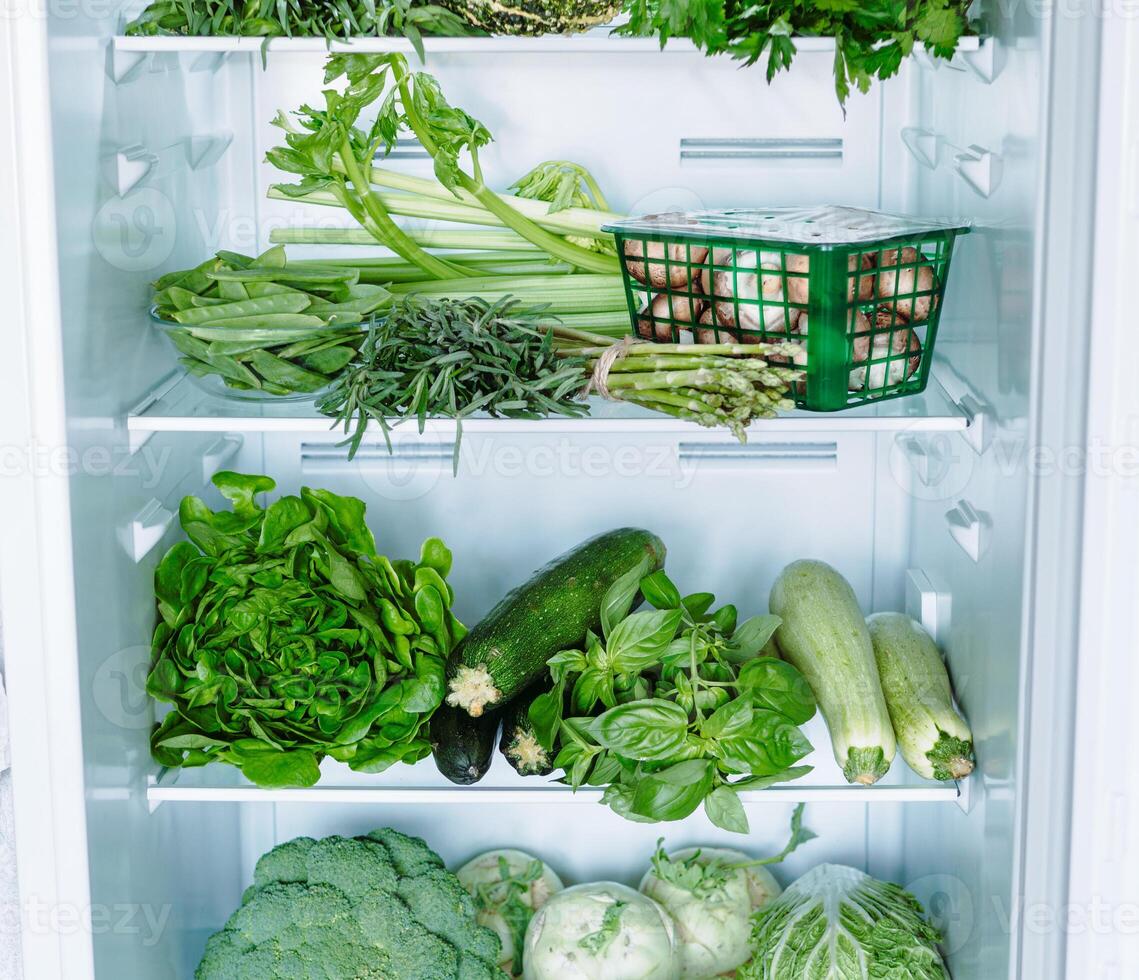 Green vegetables and greens in open refrigerator photo
