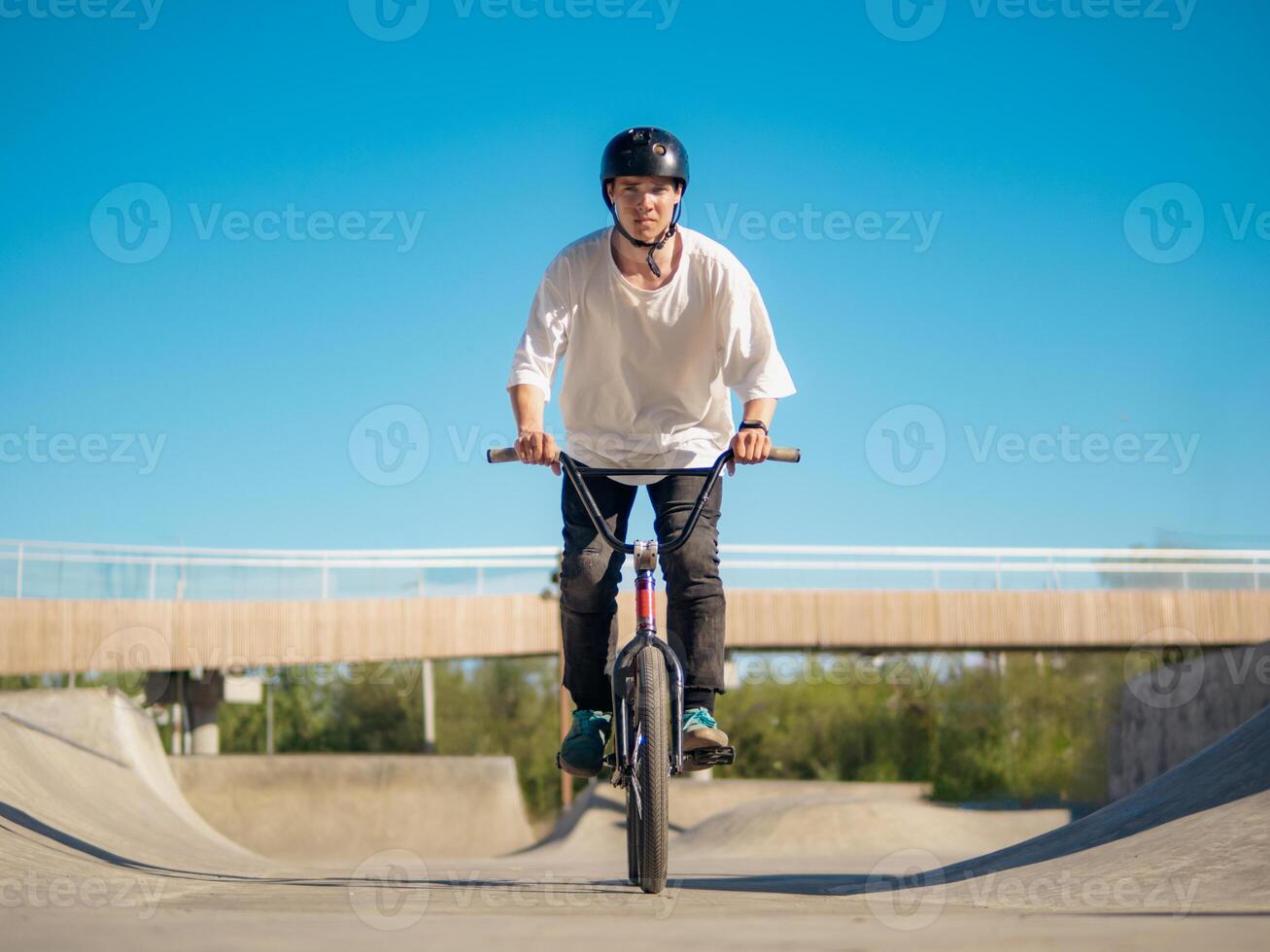 Boy rides on BMX, looking at camera in ramp park photo