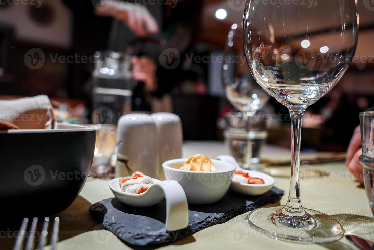 Sophisticated dining experience featuring table set with various dishes and glassware, empty wine glass dominating frame, dessert, person in background. photo