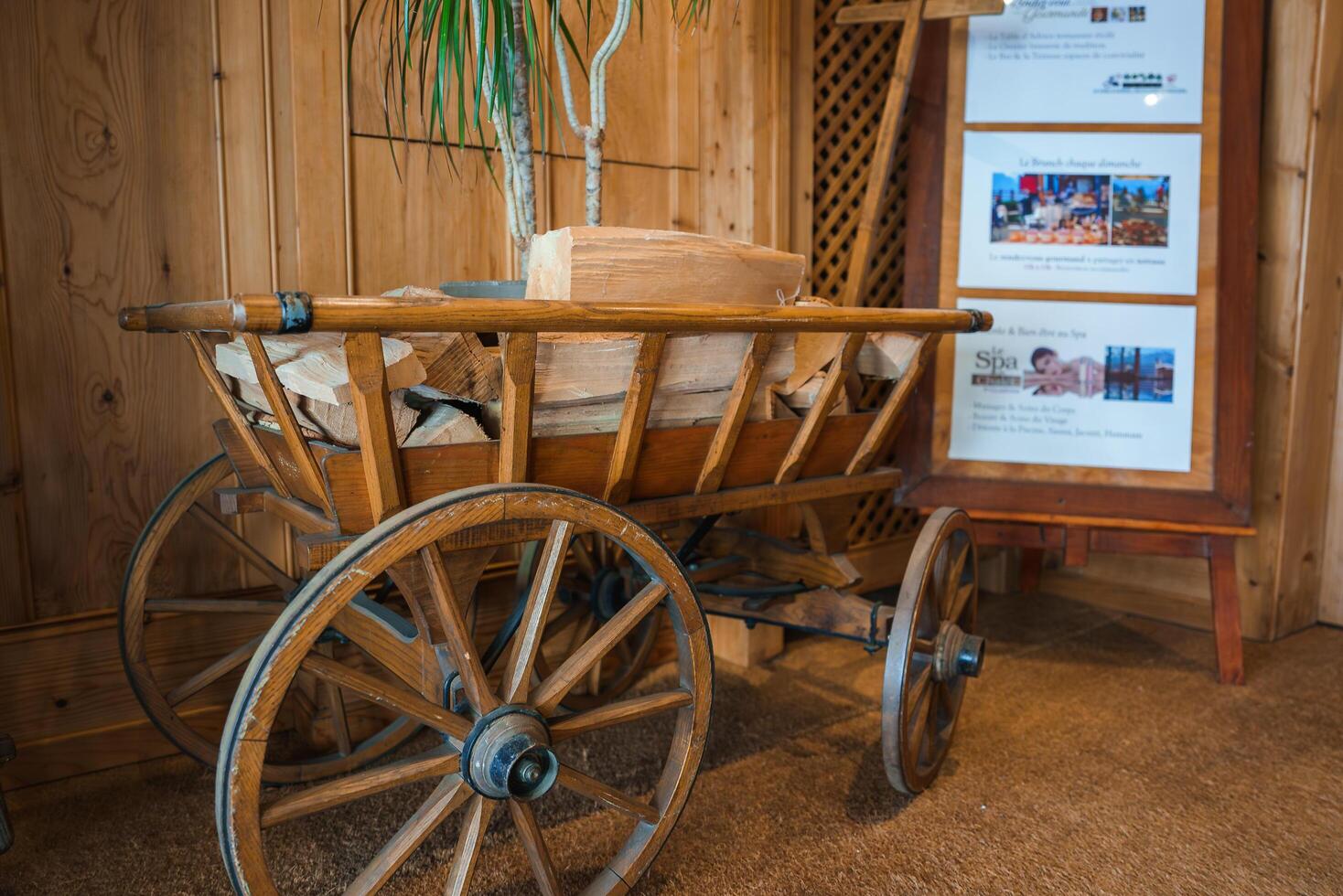 Vintage wooden cart with firewood on brown carpet indoors, hints of spa and mountain view in background, possible French speaking area resort or lodge lobby aesthetic. photo