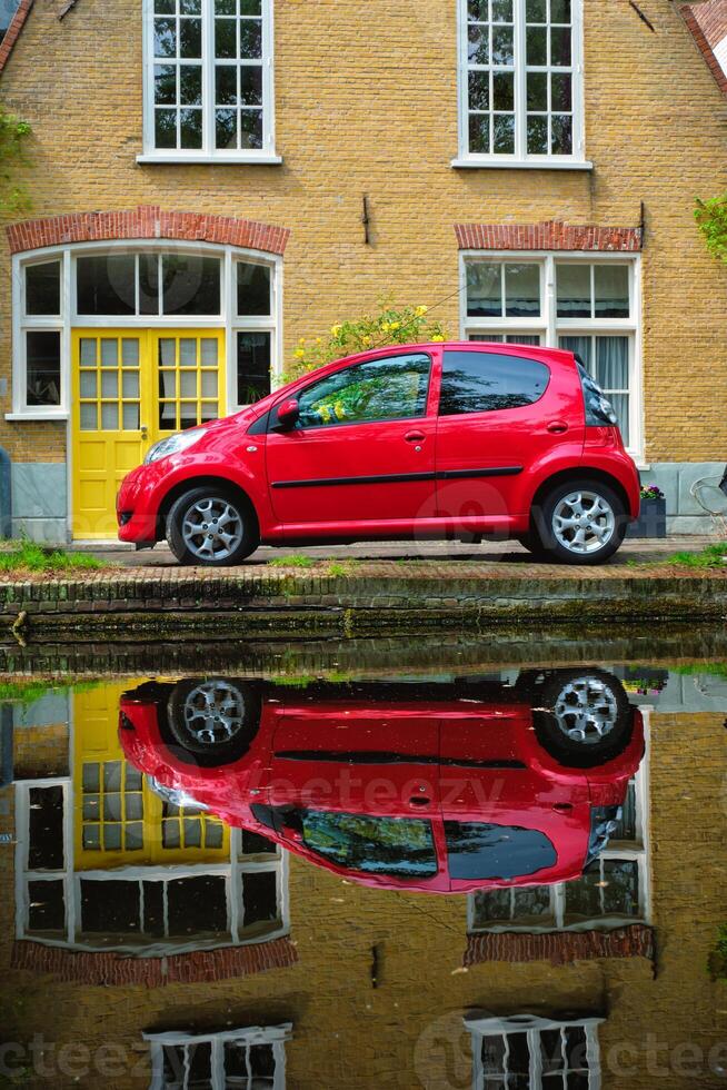 Red car on canal embankment in street of Delft. Delft, Netherlands photo