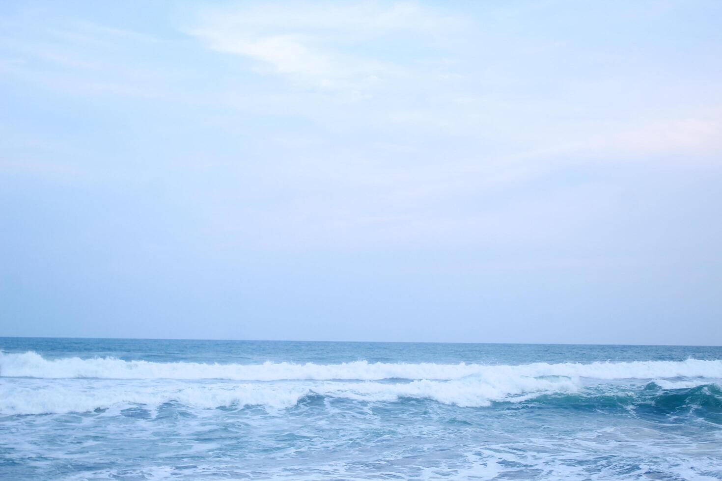 As the tide sweeps in at South Jogja Jetis Beach, Cornwall under a serene sky, waves gently roll, accompanied by ripples and bubbling foam. photo