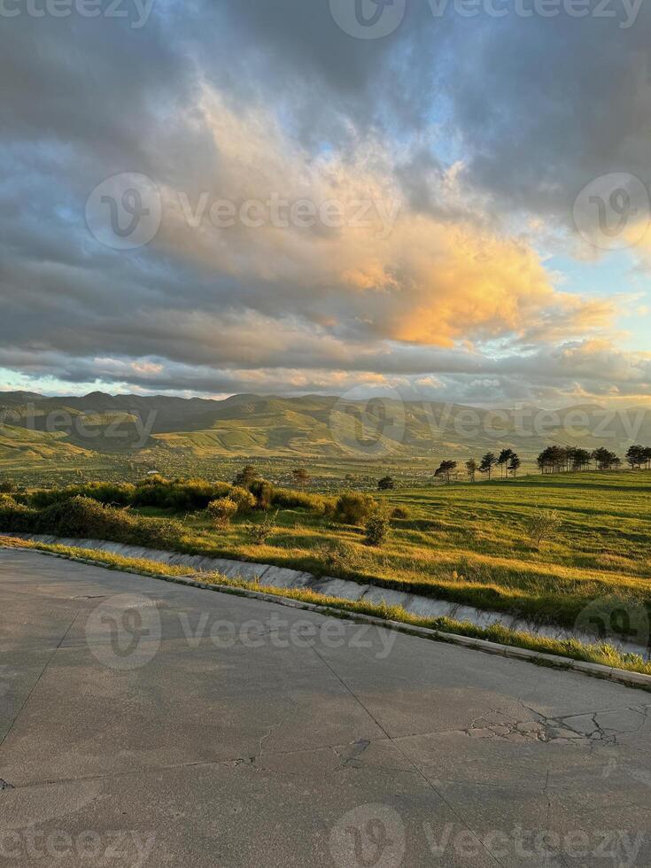Landscape on sunset with green field of grass with mountains under clouds photo