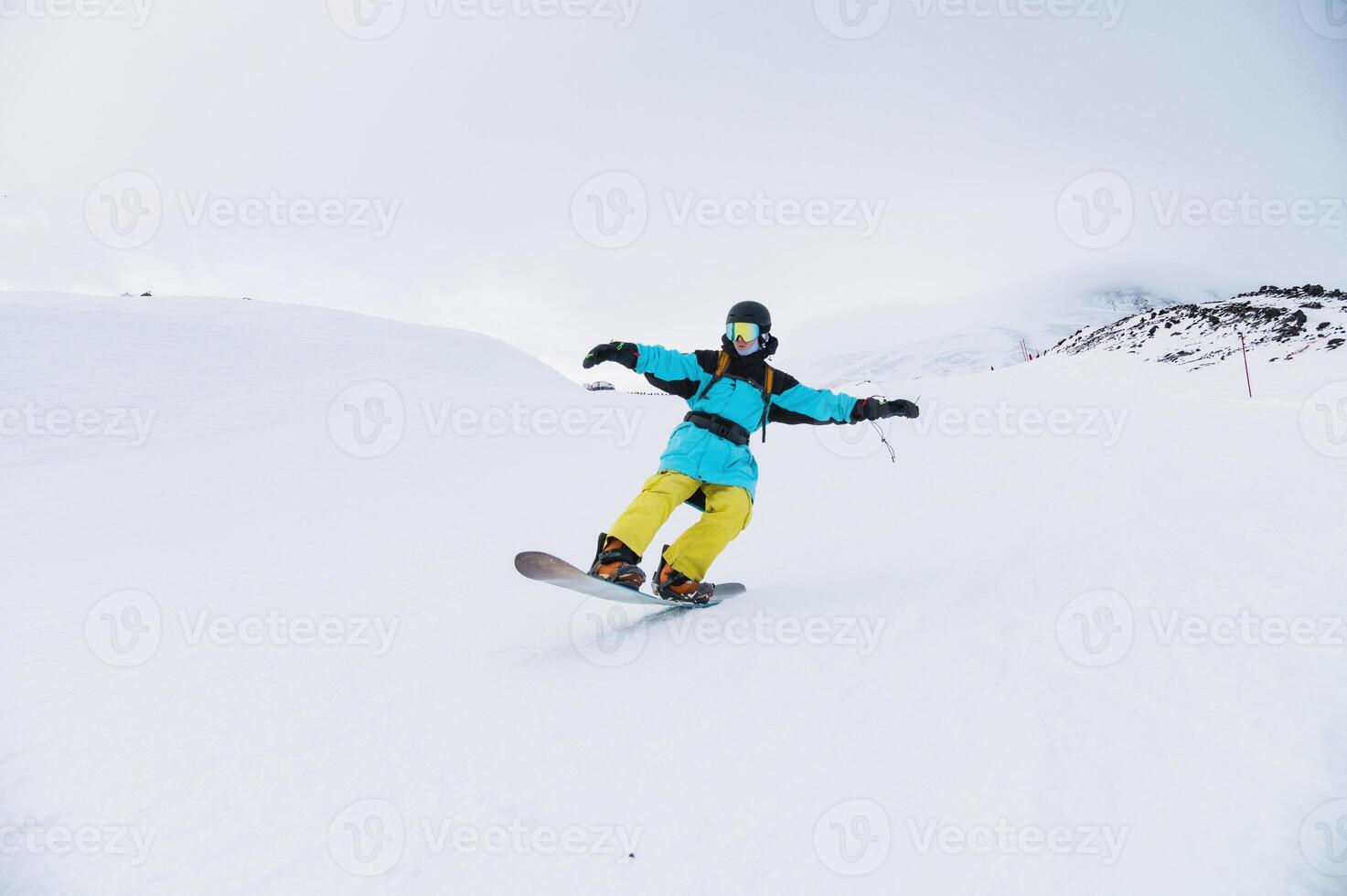 snowboarder rides down the slope of a ski resort in a helmet and protection, doing a trick on the snow photo