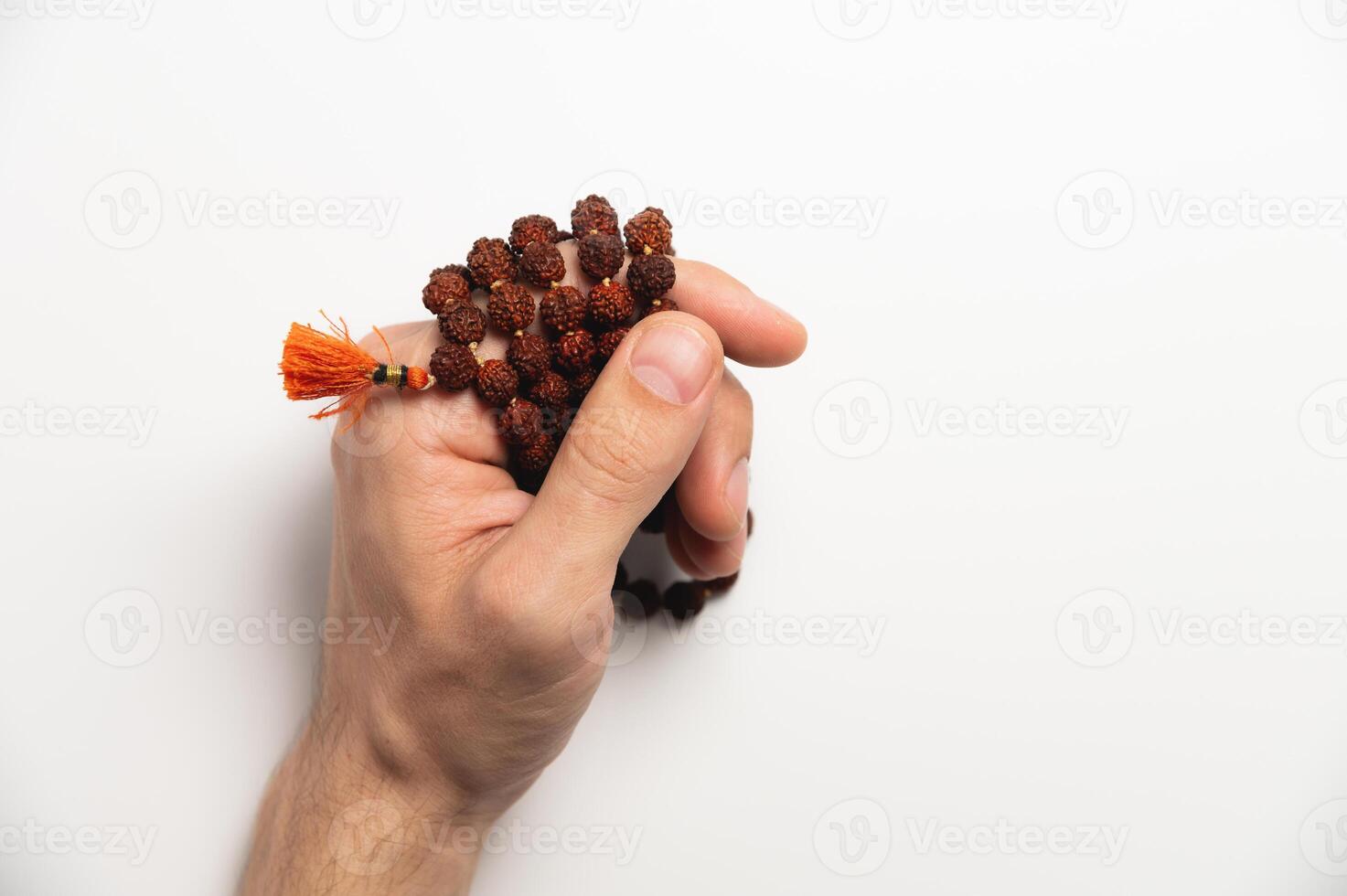 Hand of a praying man holding a rosary, with a red brush at the end, on a white background close-up photo