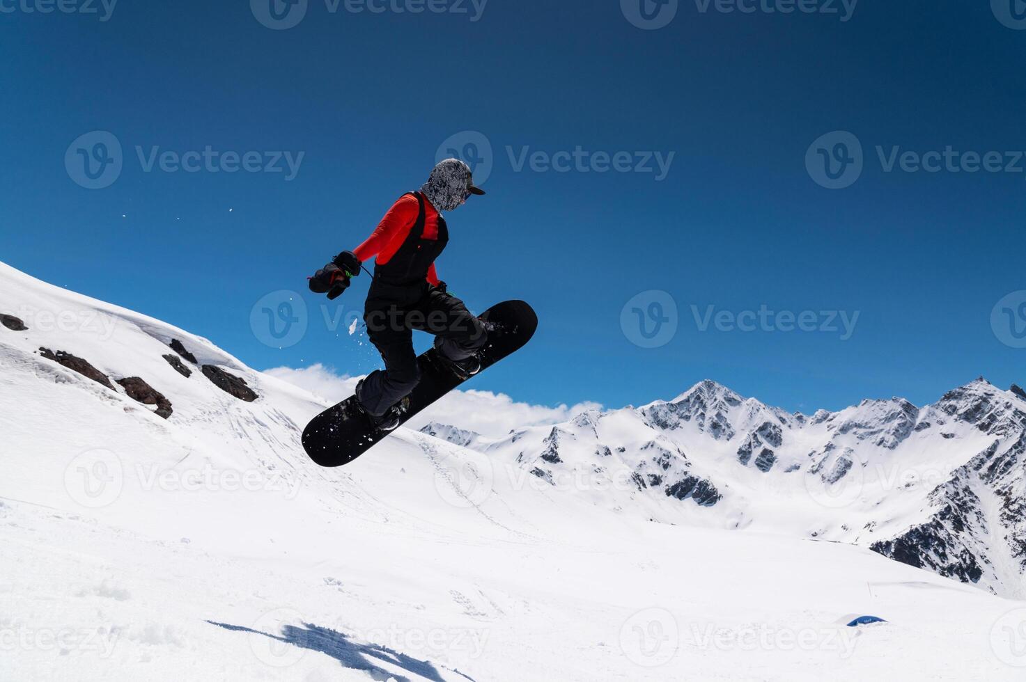 snowboarder in bright sportswear makes a trick against the backdrop of beautiful mountains photo