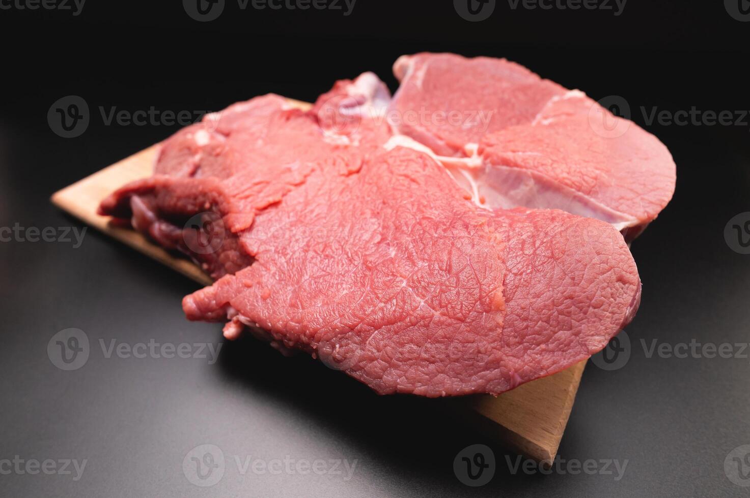 piece of raw beef in a slice on a wooden cutting board, on a black background. Procuring food photo