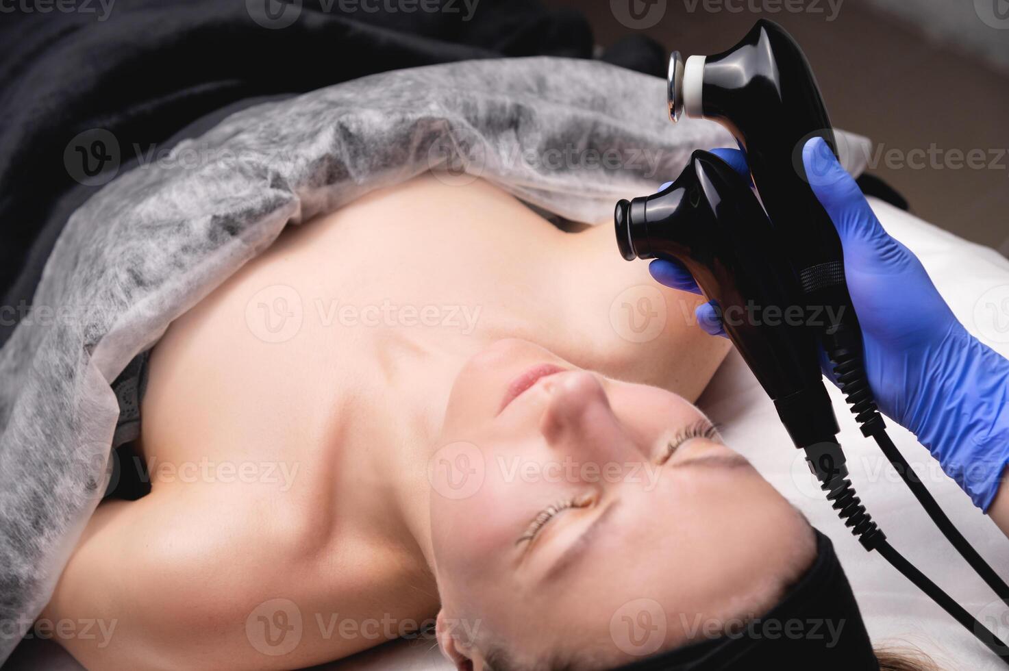 Young woman undergoing facial rejuvenation procedure with tekar therapy in salon, top side view, close-up photo
