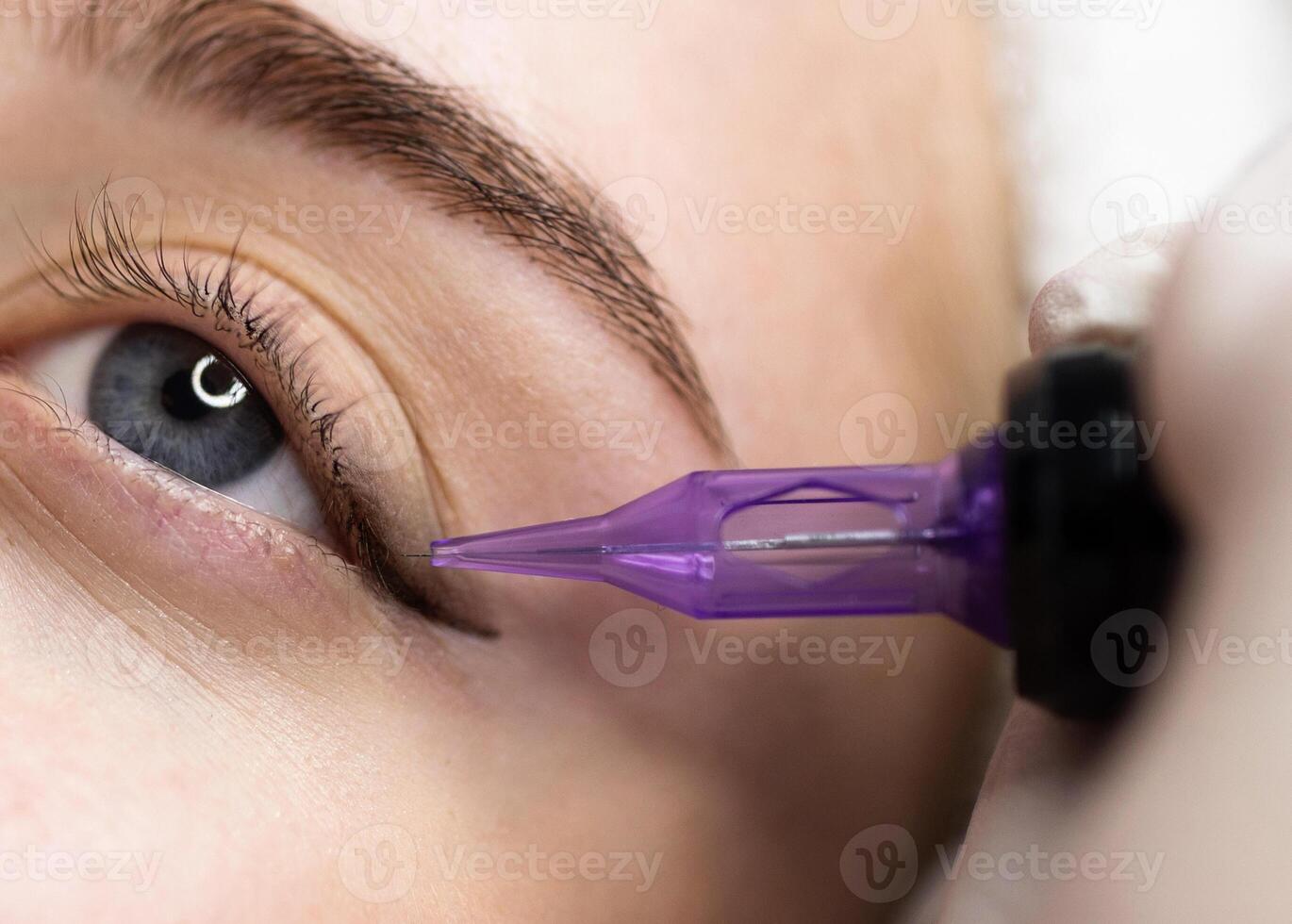 Micropigmentation Concept. Beautician doing permanent make up eyeliner procedure to young woman, closeup of attractive female getting pmu treatment in beauty studio, artist using tattoo pen machine photo