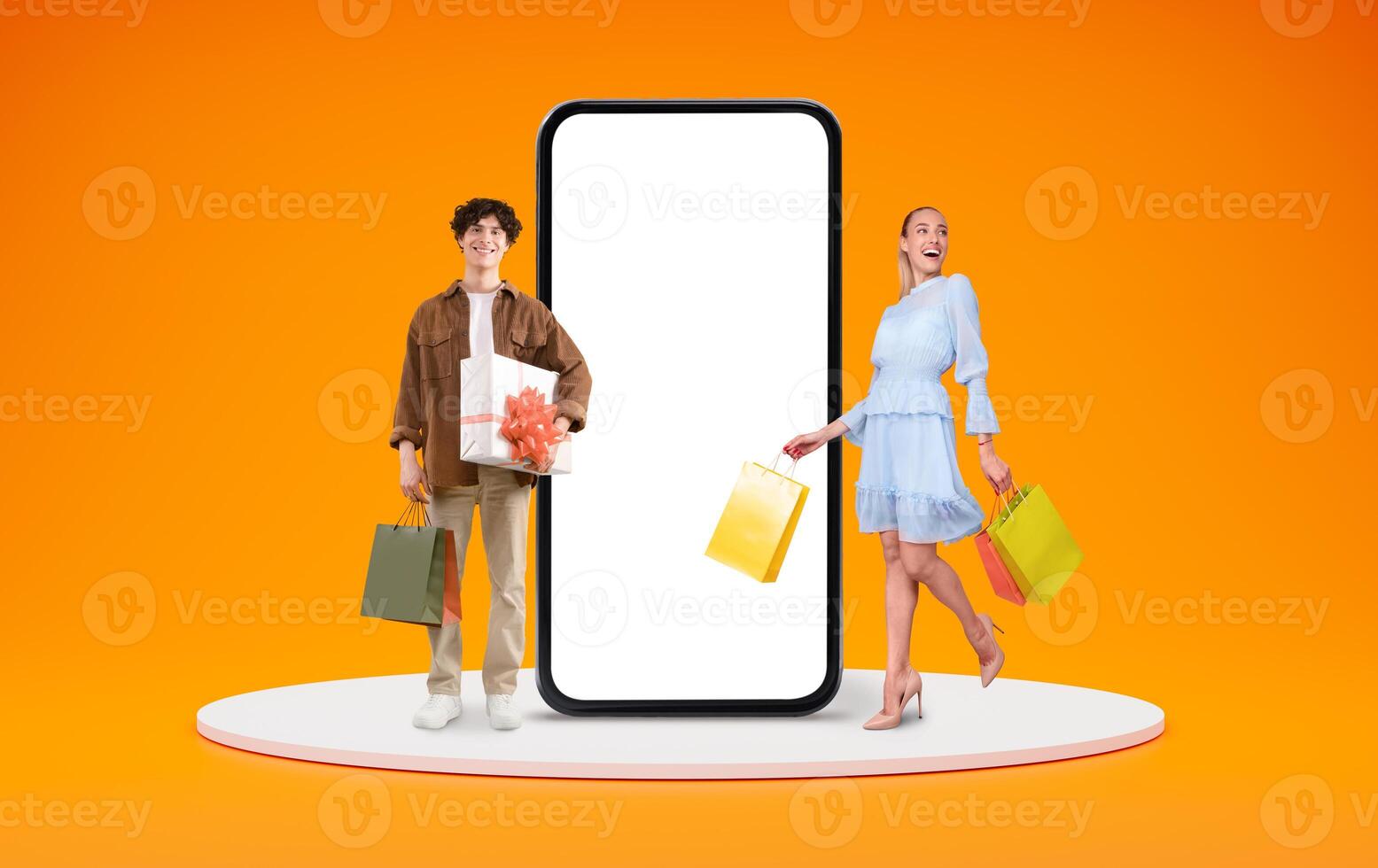 Online Shopping App. Cheerful young man and woman standing near big blank smartphone with white screen and holding bright shopper bags, happy customers posing isolated over orange background, mockup photo