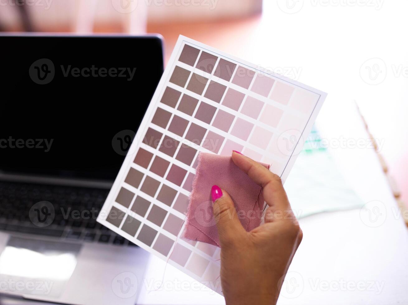 Color Choice In Fashion Design. Closeup Of Female Hand Near Laptop Computer Holding Brown Colors Shades Palette And Fabric Sample At Modern Clothing Design Studio. Cropped Shot photo