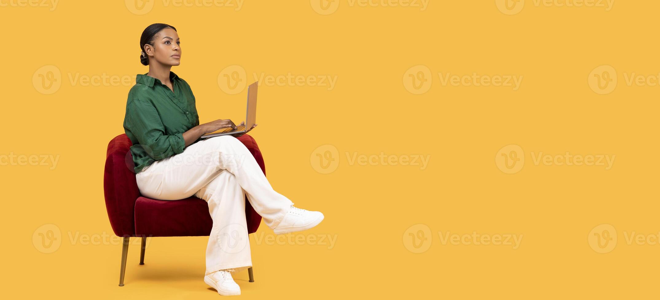 Internet Offer. Thoughtful Black Lady Freelancer Browsing Web On Laptop Sitting In Red Armchair With Computer On Lap, Looking Aside At Copy Space For Advertisement On Yellow Background, Panorama photo