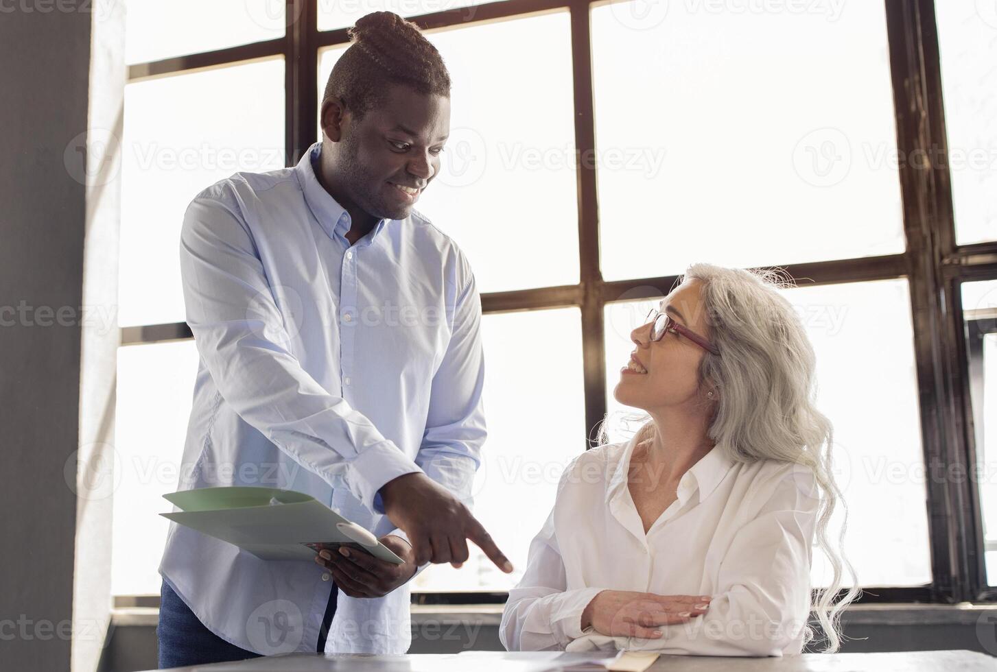 Mentorship At Workplace. African American Businessman Providing Guidance and Support to Employee Woman As Coworker Starting Her New Job, Pointing Finger On Table In Office Indoors photo