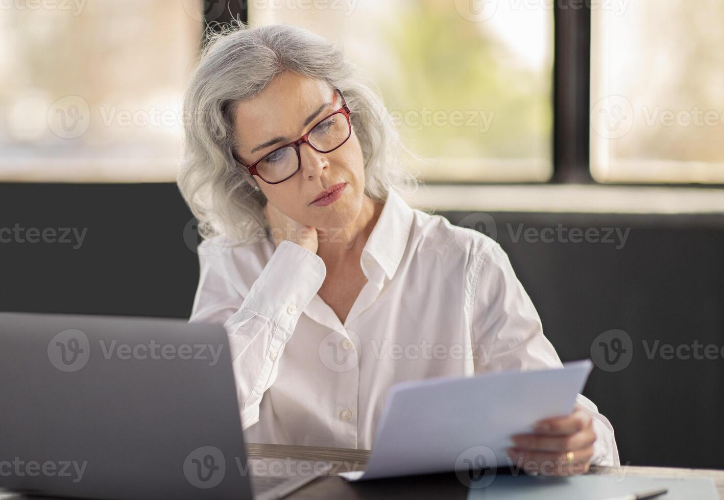 Business Paperwork. Businesswoman Reading Papers Wearing Eyeglasses, Sitting At Laptop Computer In Modern Office. Professional Manager Looking Through Documentation, Bills And Correspondence photo