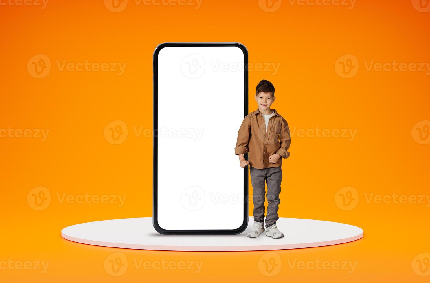 Educational kids mobile app. Happy positive cute little boy standing by big smartphone with black white screen and smiling, ready for school, posing over orange studio background, copy space photo