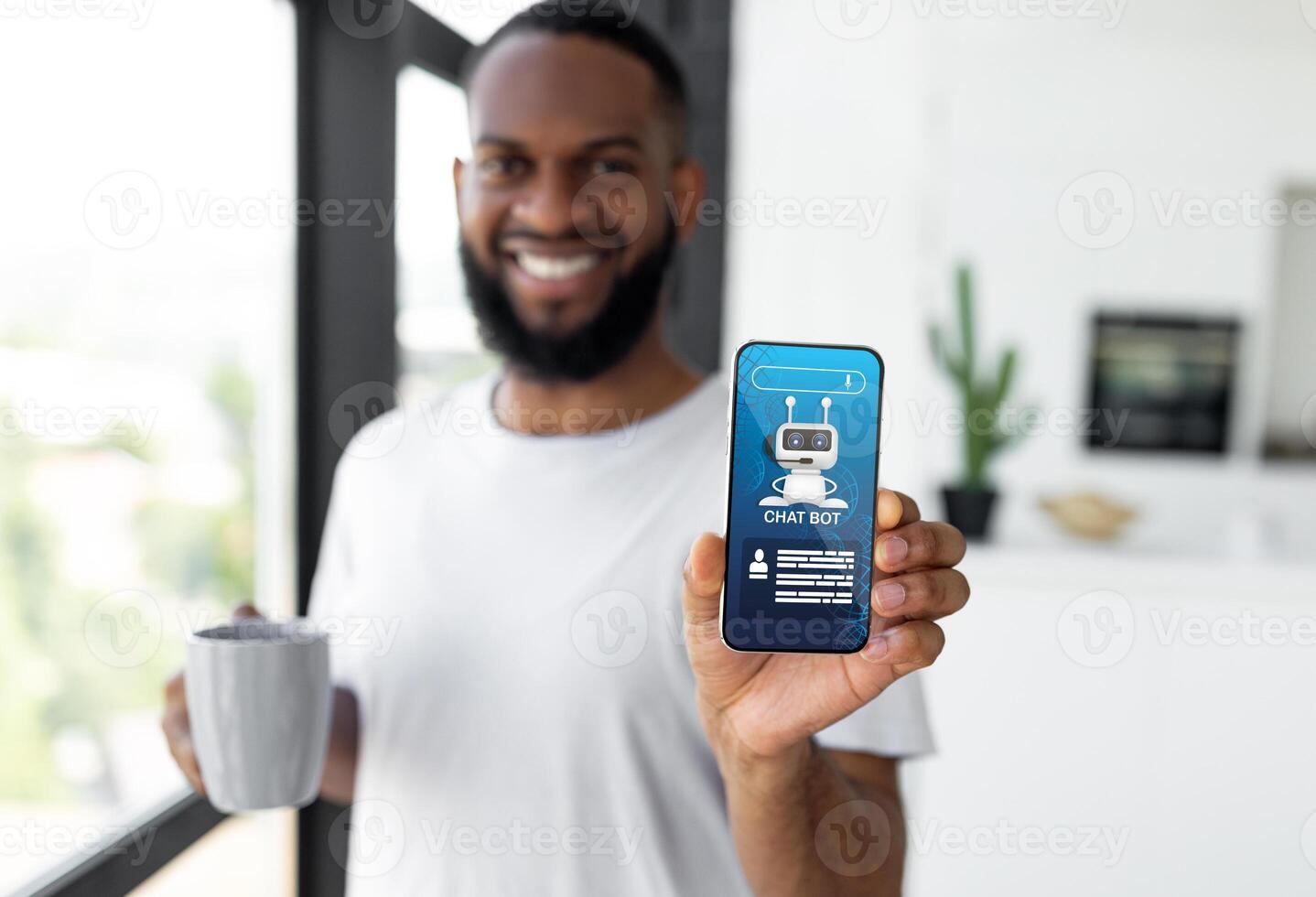 Cheerful handsome young black guy in white t-shirt, drinking coffee, showing cell phone with chatbot icon application on screen, home interior. Artificial intelligence, AI in daily life, collage photo