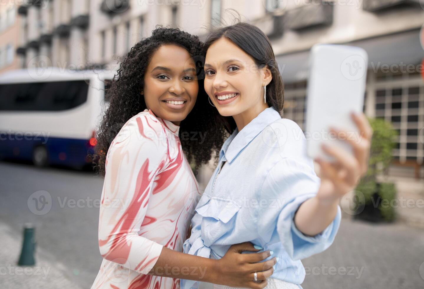 Two Cheerful Female Friends With Smartphone Taking Selfie While Walking Outdoors, Happy Young Multiethnic Girlfriends Making Photos Together, Joyful Besties Having Fun And Smiling At Camera