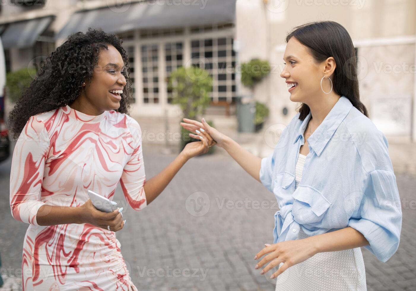 Portrait Of Two Cheerful Multhiethnic Female Friends Laughing And Chatting Outdoors, Joyful Beautiful Young Girlfriends Meeting On City Street, Happy To See Each Other, Having Fun Outside photo