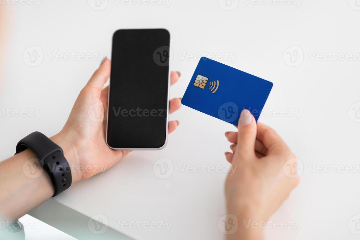 Hands of young european woman use smartphone with blank screen and credit card on white table in office, cropped. Banking, business and work, device and shopping, sale app, order and pay photo