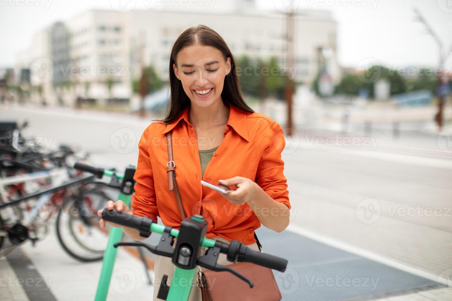 Smart Public Transportation. Happy Young Woman Renting Electric Scooter Unlocking Eco Transport Via Smartphone Application Standing At Bike Park On A Street In Urban Area Outdoors photo
