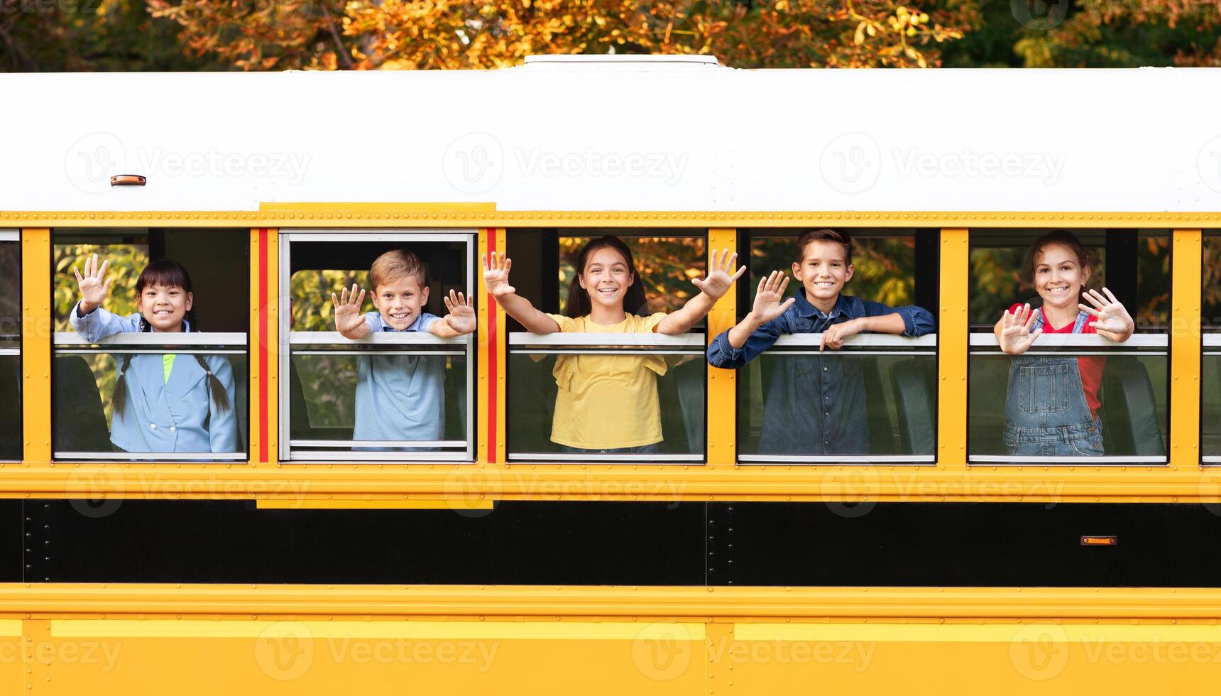 Group Of Happy Kids Waving Hands While Peeking Out Of School Bus, Cheerful Multiethnic Children Enjoying Trip Together, Getting Home After Lessons, Looking Out Of Window And Smiling, Free Space photo
