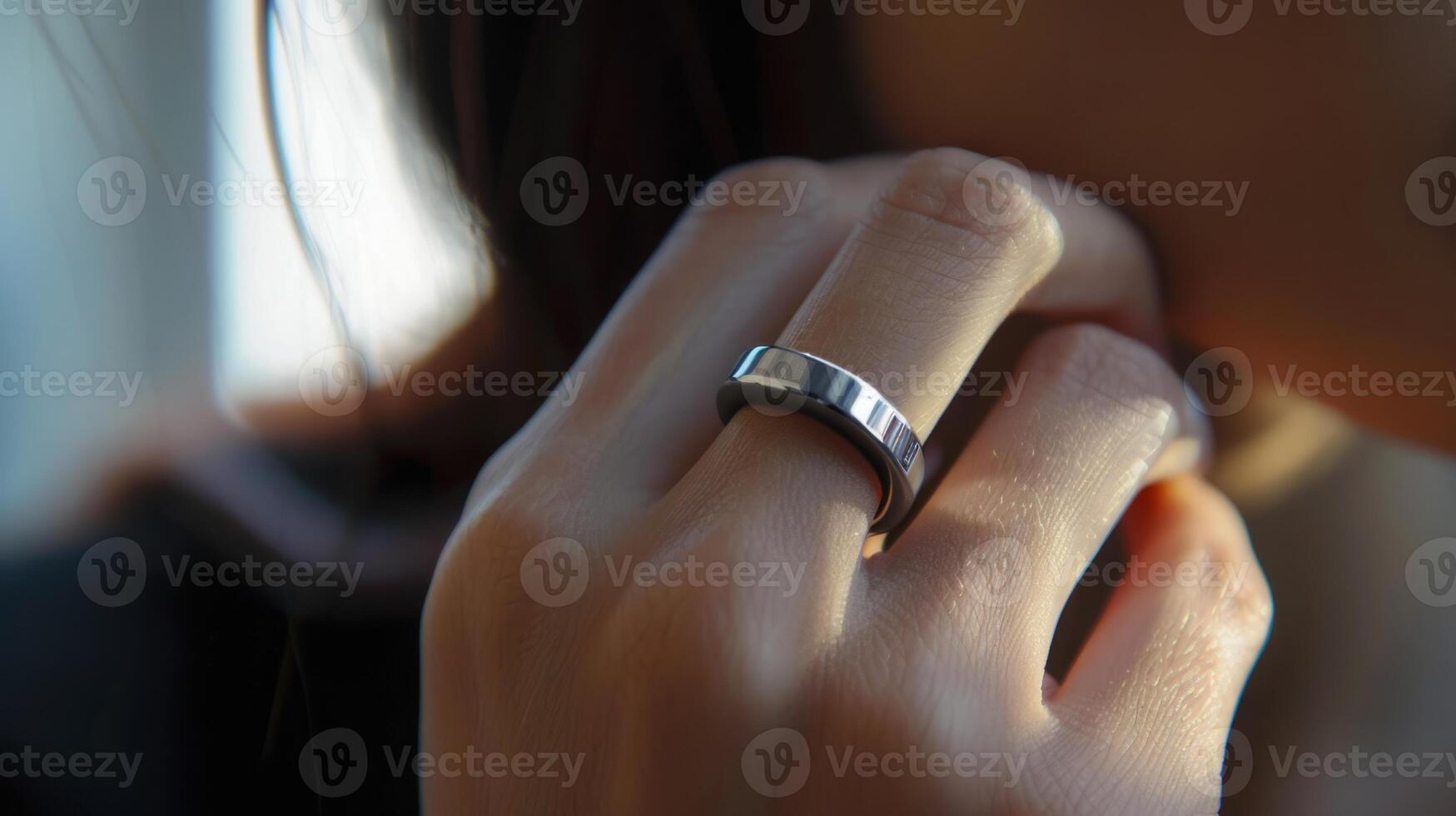 A close-up view of a womans hand with a silver ring on her middle finger. The ring is simple and stylish, with a smooth surface and a slightly rounded edge. The womans skin is soft and pale, and the light reflects off the metal of the ring. photo