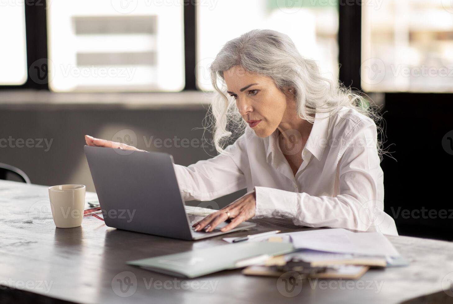 Office Work Routine. Determined Middle Aged Businesswoman Working On Laptop Computer, Typing And Solving Difficult Tasks Problems At Workplace Indoor, Sitting At Table Indoors photo