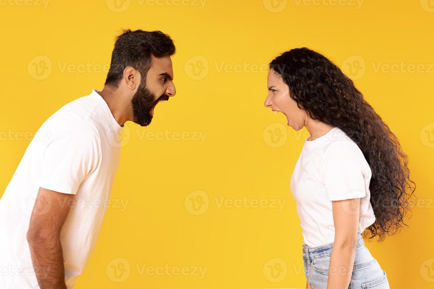 Family Problems, Conflicts. Mad Arabic Couple Shouting At Each Other Having Quarrel Standing On Yellow Background. Side View Of Angry Young Spouses Freaking Out And Yelling Loudly During Scandal photo