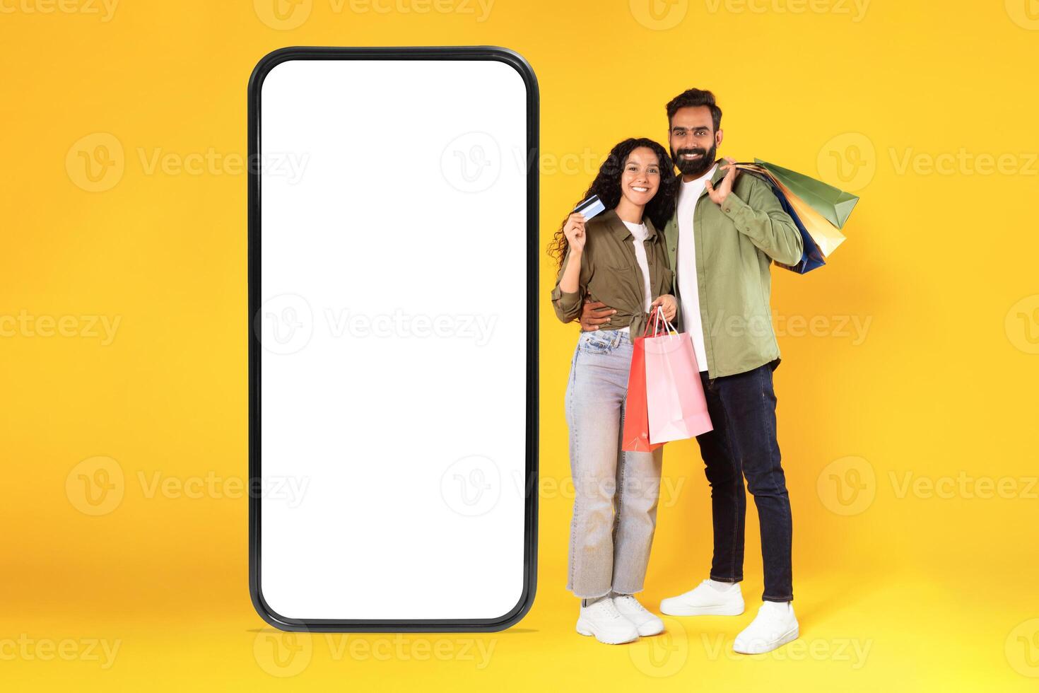 Sales Ad. Happy Arabic Buyers Couple With Shopping Bags And Credit Card Embracing Near Huge Smartphone With Empty Screen, Smiling At Camera Posing Over Yellow Studio Background. Collage photo