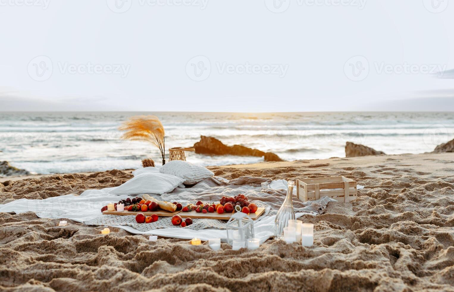 Having picnic with fresh fruits and rose wine on blanket at sandy beach over sea shore at background, free space. Summer season. Vacation time. photo
