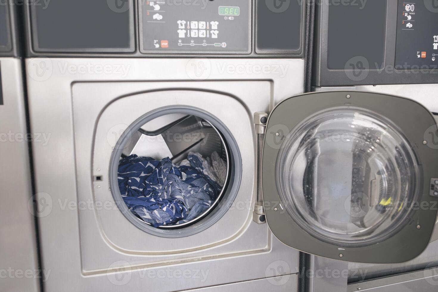 Public Laundry. Shot Of Modern Industrial Washing Machine With Opened Door And Loaded Clothes At Laundrette Indoors. Public Convenience Service, Automatic Laundromat Room Concept photo