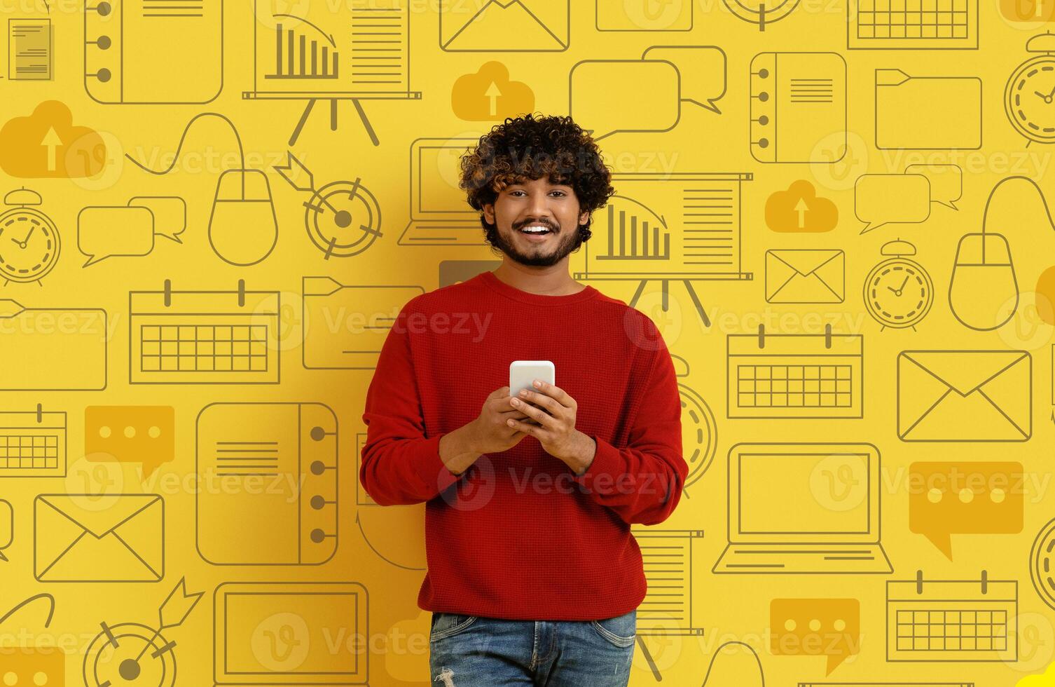 Happy young handsome hindu man in casual with phone in hands posing over diverse digital world icons on yellow background. Concept of modern technologies, mobile applications, chat gpt concept photo