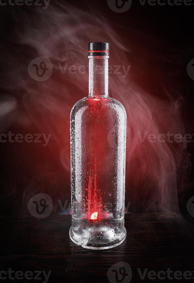 A wet bottle on a beautifully illuminated background. Smoke around a glass bottle. photo