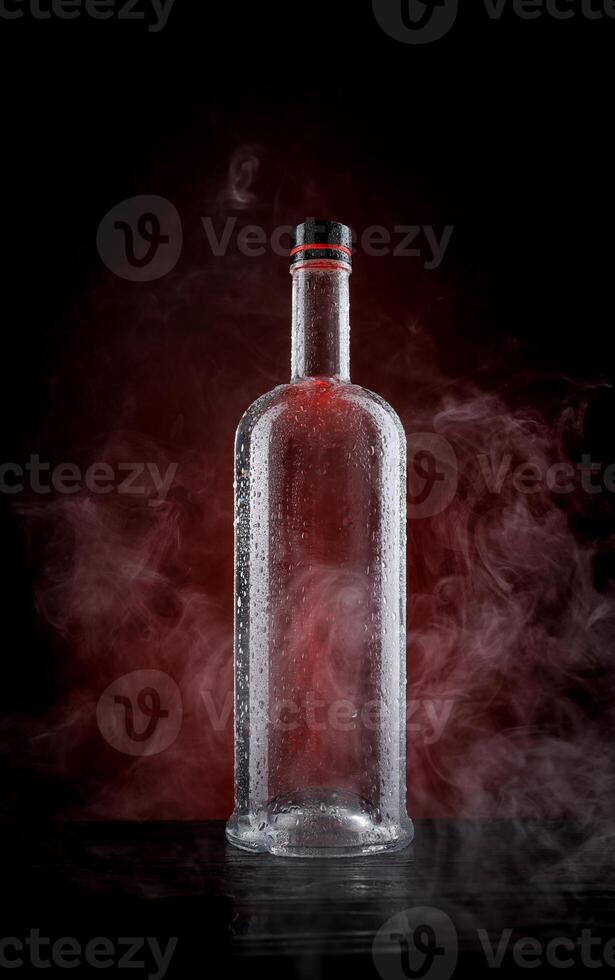 A wet bottle on a beautifully illuminated background. Smoke around a glass bottle. photo