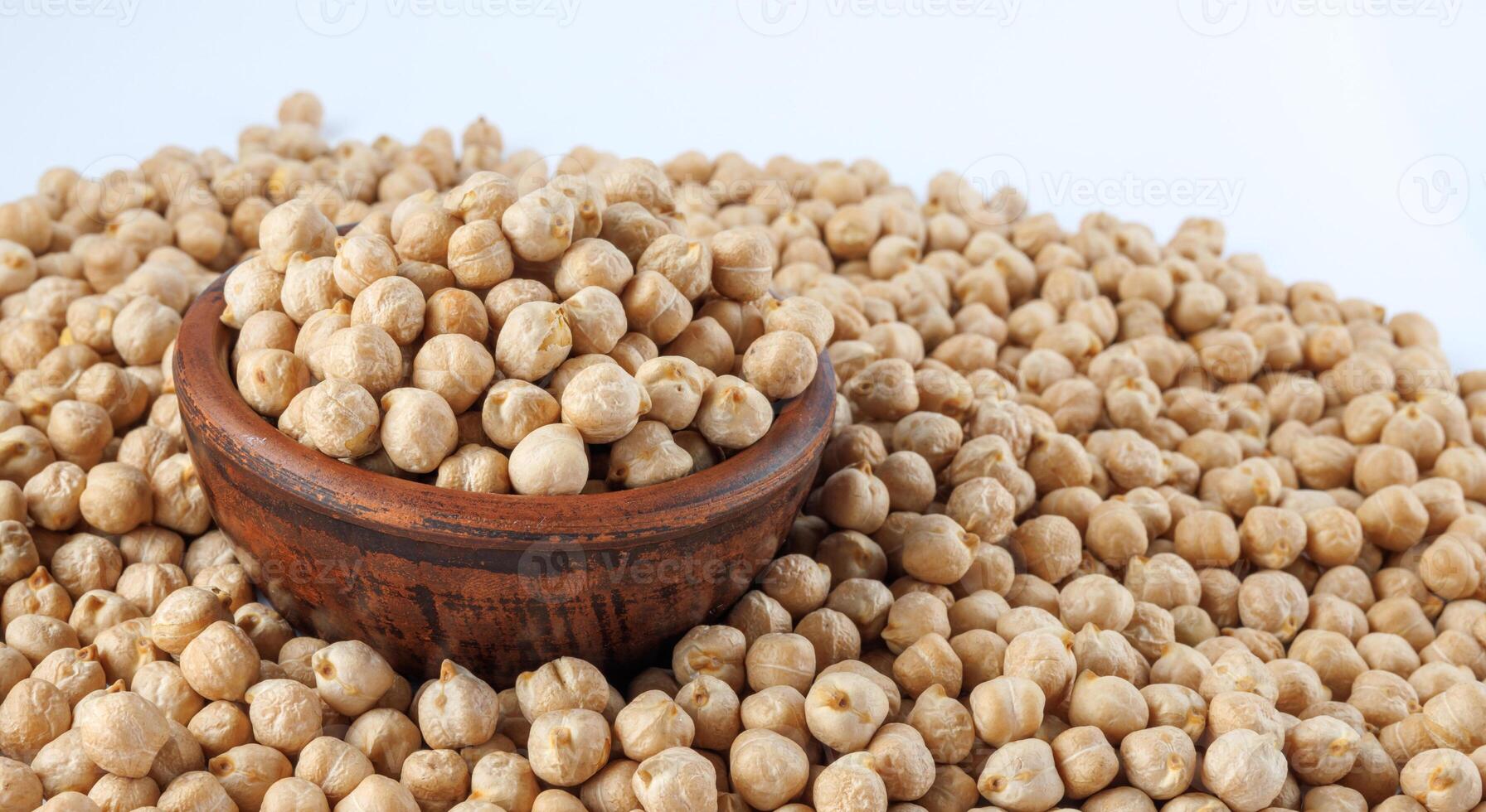 A clay bowl full of chickpeas stands in a pile of scattered chickpeas. Heap of chickpeas on a white background. photo