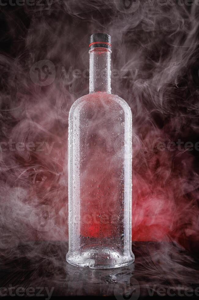 A wet bottle on a beautifully illuminated background. Smoke around a glass bottle. photo